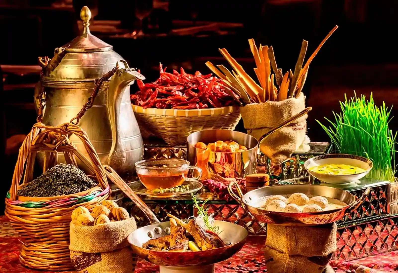 A Kashmiri spread laid out on a carpet: a brass samovar, dried red Kashmiri chillies, cinnamon bark, walnuts, a cup of kahwa, tabak maaz ribs and a copper pan of gushtaba in white gravy.