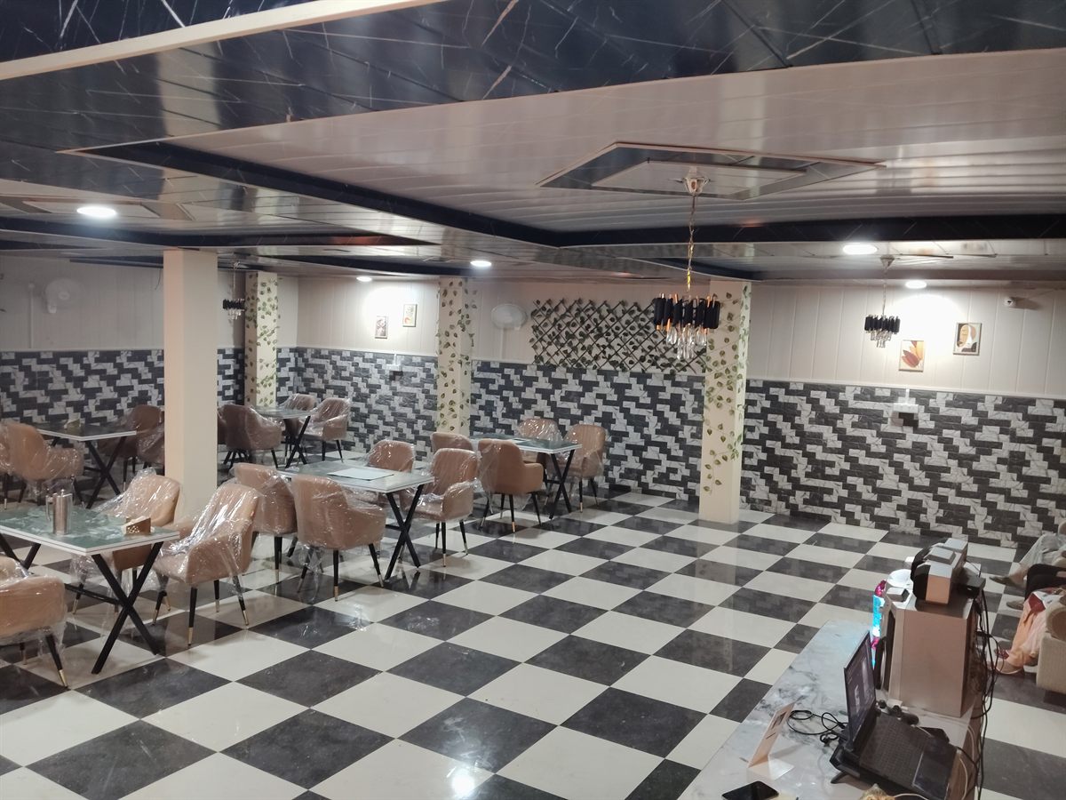 The main dining hall: blush upholstered chairs around marble-topped tables on a black and white checkerboard floor, under a panelled ceiling.